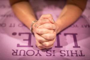 hands folded on a purple yoga mat
