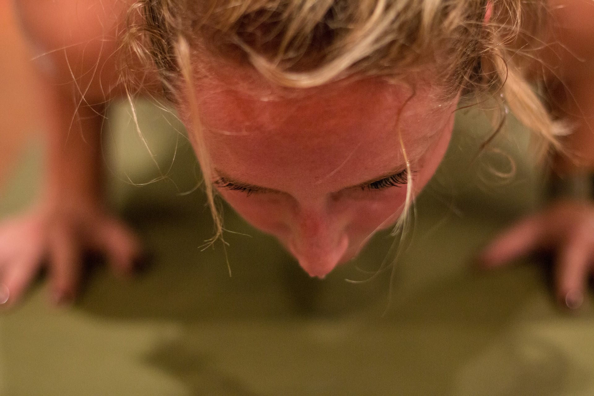 female yoga student in push up position with sweat dripping off of nose